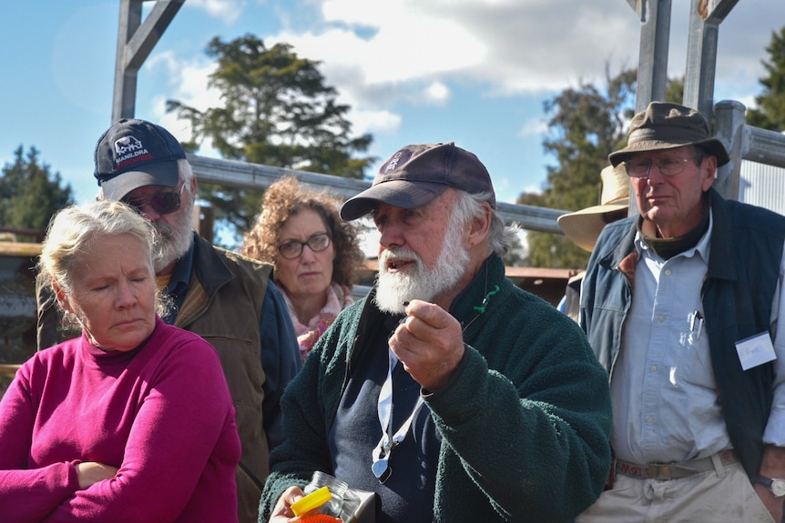 A man with a white beard holds a dung beetle in front of a group of farmers.