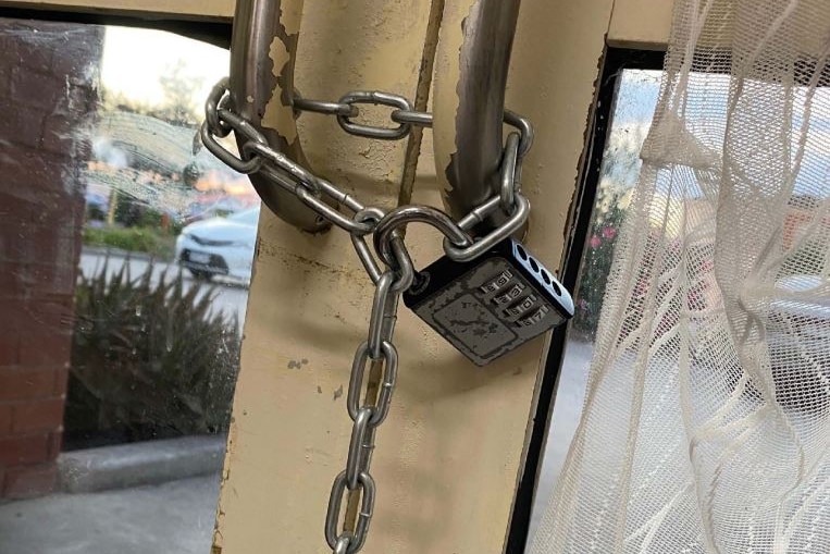 A chain with combination lock secure from the inside, two entryway doors on a building.