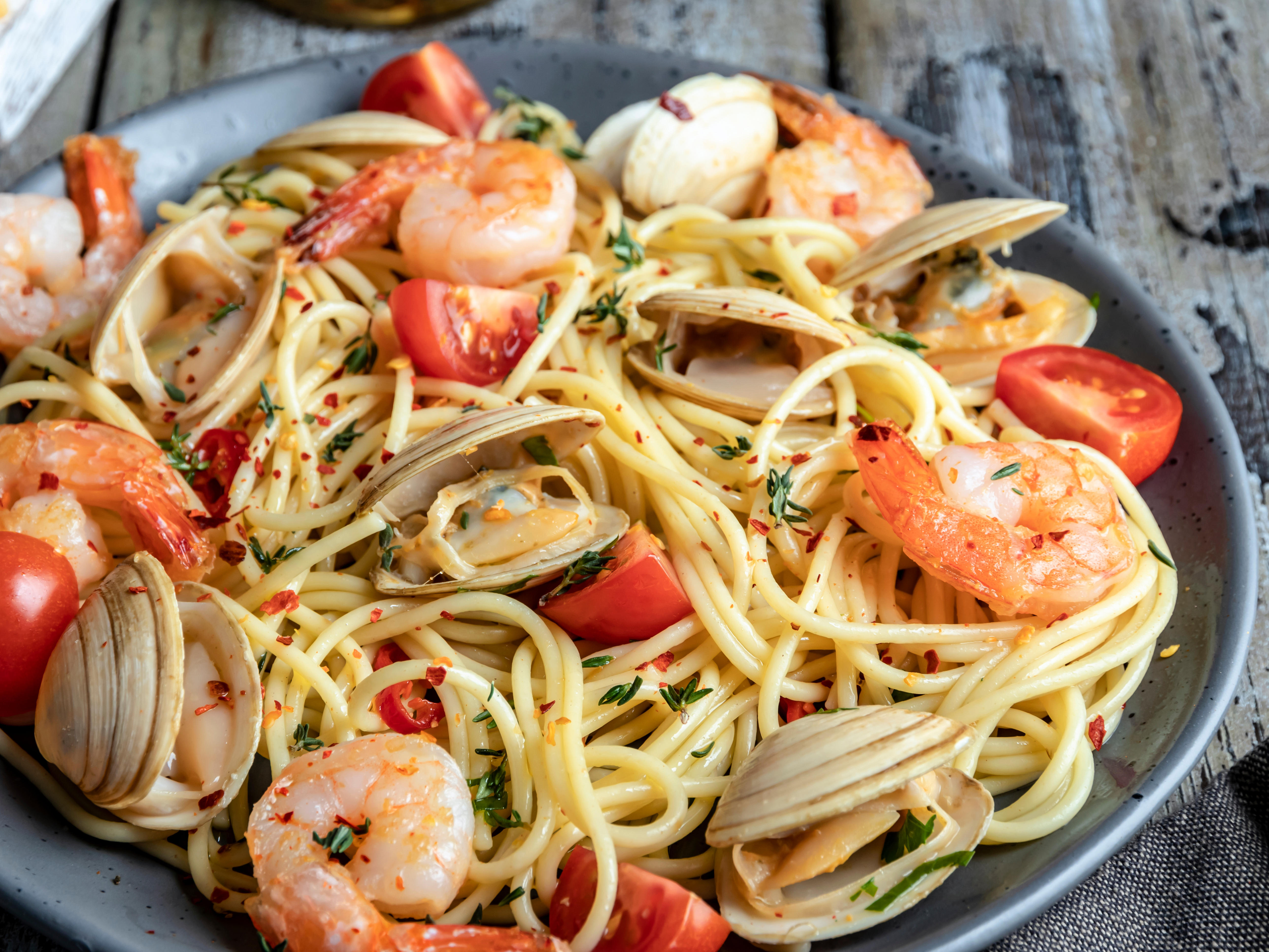 Cooked spaghetti with pipis, prawns and tomato on a plate.