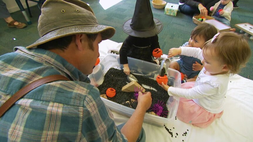 The back of Gardening Australia presenter Tino Carnevale's head with children dressed in costume in front on him