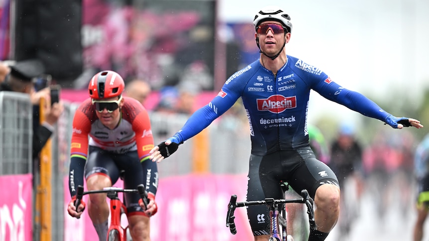 Kaden Groves (right in blue) extends his arms after crossing the finish line on sage five of the Giro d'Italia.