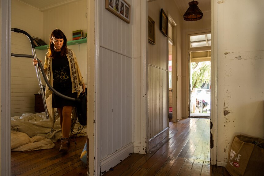 a woman inside a room in a house holding a vacuum cleaner