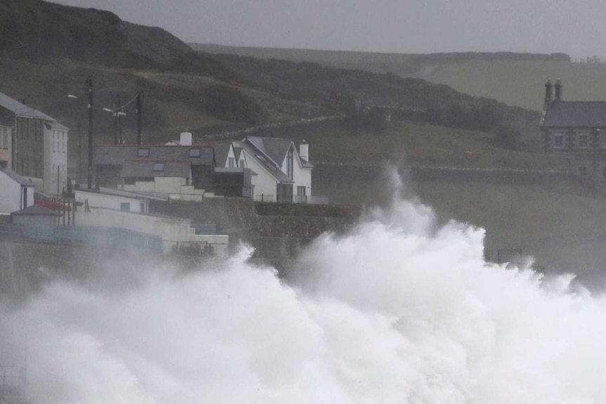Big waves crash into the coastline in southwest England, very close to houses.