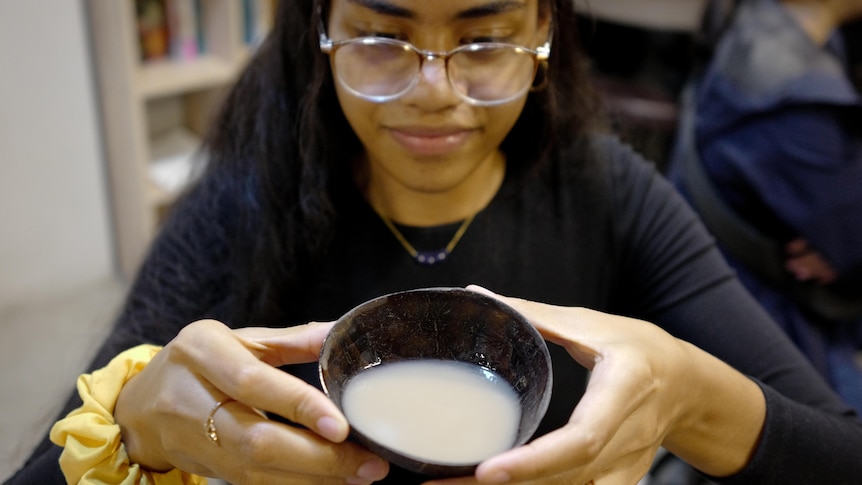 A young woman holds a bowl of kava. 