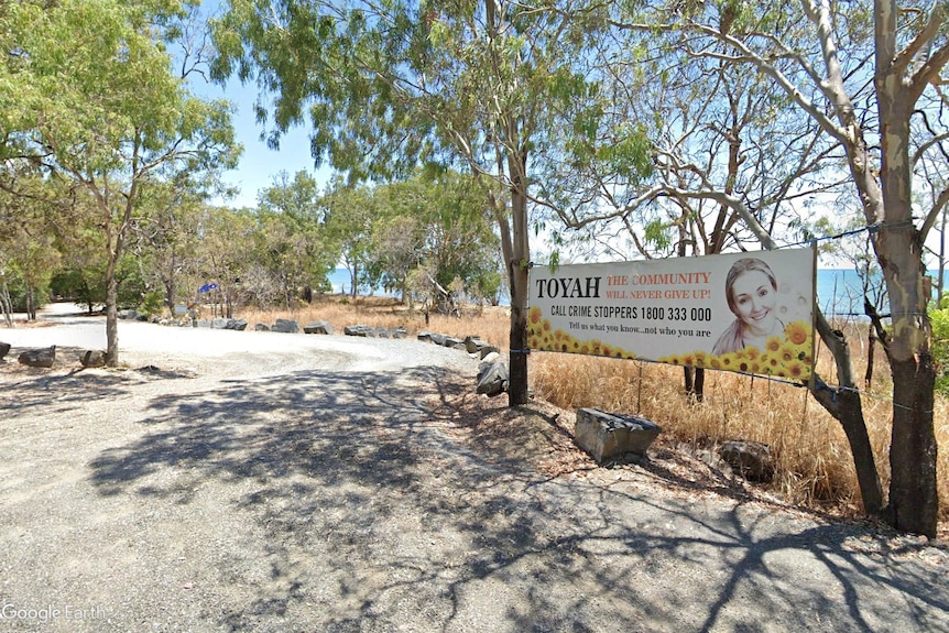 A banner with a young woman's face, sunflowers and TOYAH in big bold letters is hung in a car park by the beach