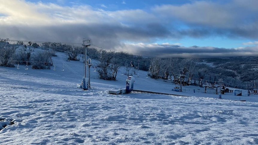 A landscape picture of a snow-covered hill at a ski resort, with blue sky and cloud visible in the background