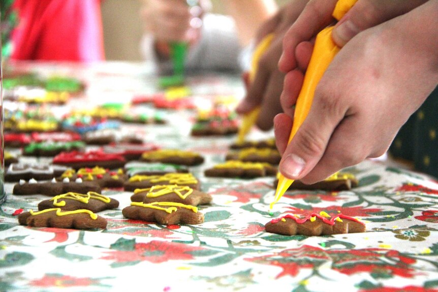 Children using yellow icing to decorate gingerbread biscuits