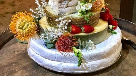 five layers of cheese stacked on top of each other to look like a cake with flowers and fruit placed on top of it.