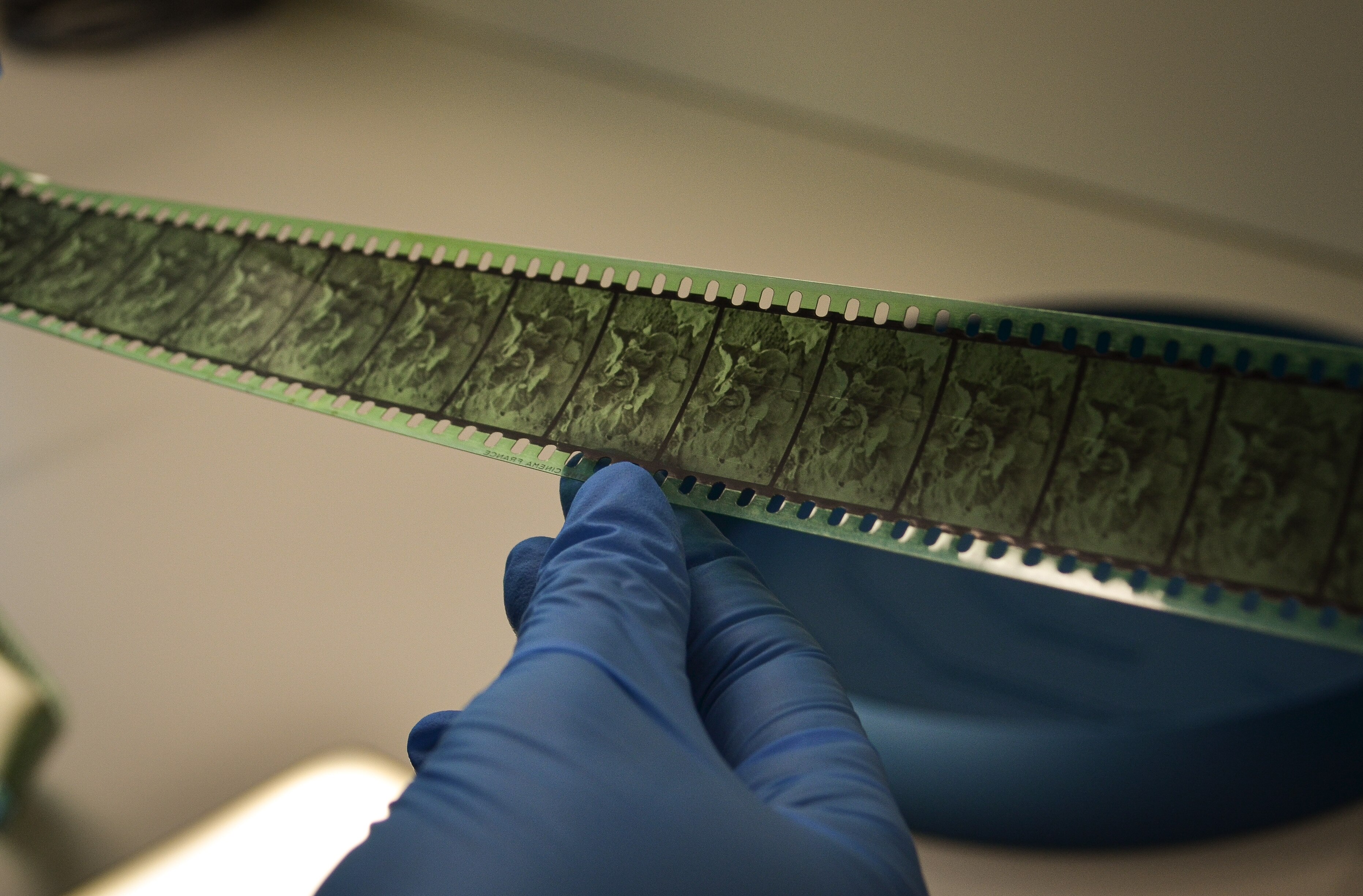 The black and white reel of film is green tinged, and is being held by a hand wearing a blue-purple rubber glove