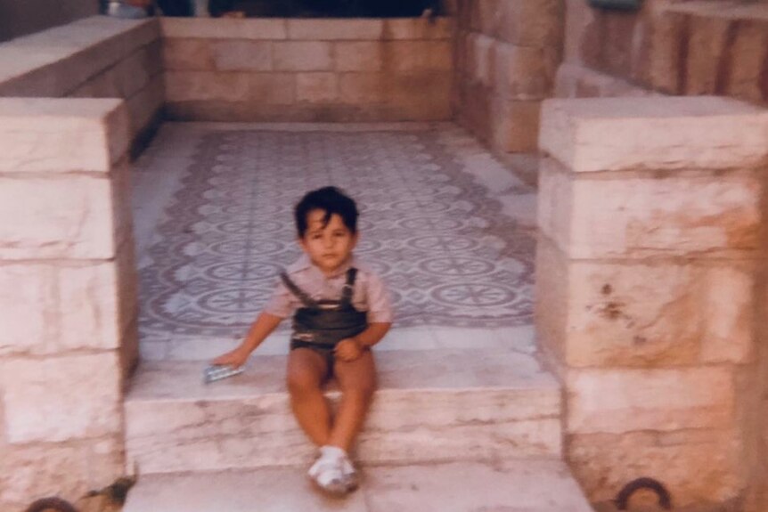 a young boy in overalls sits on marble steps