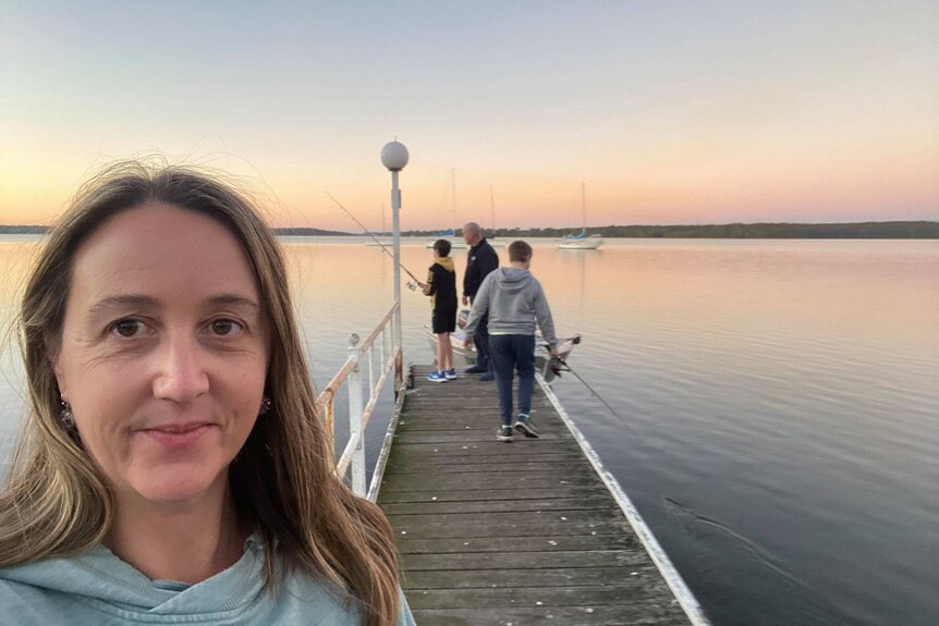 A woman takes a selfie with her family in the background.