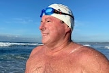 Swimmer with white cap and goggles on a beach.