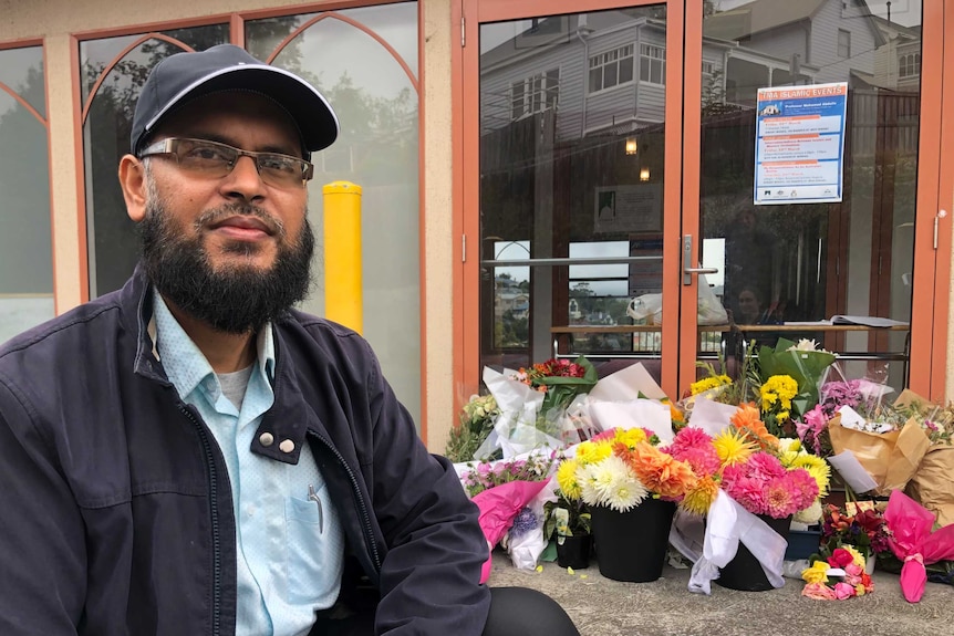 Kazi Sabbir kneels in front of floral tributes