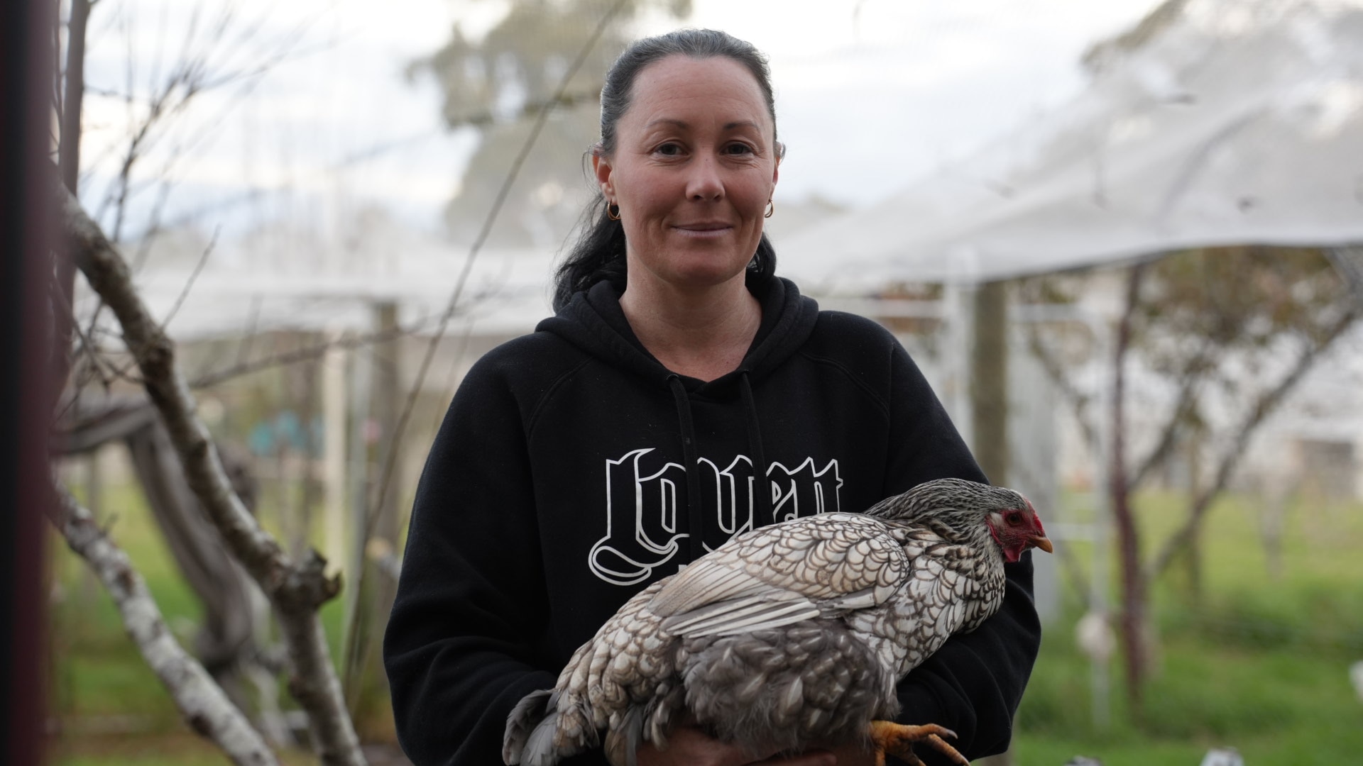 A woman is holding a chicken. 