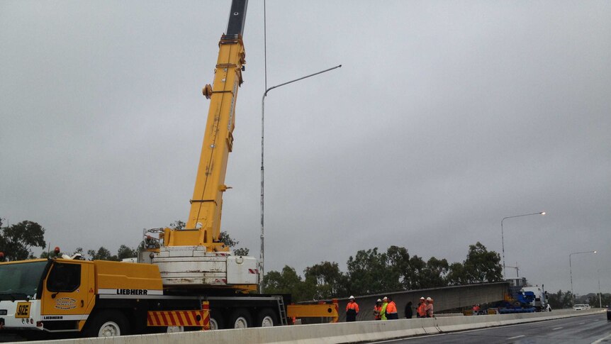 A crane prepares to lift the load from a semi trailer that jackknifed on the Neville Hewitt Bridge.