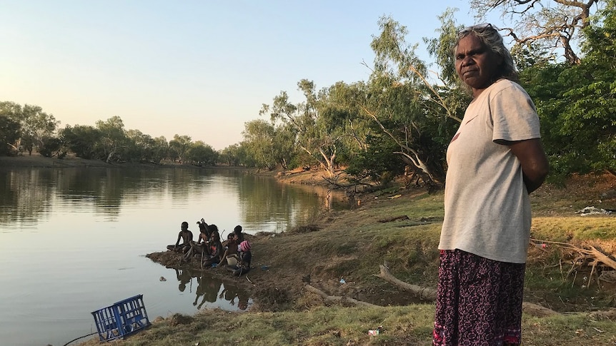 Naomi Wilfred stands by a river, as children sit on the banks