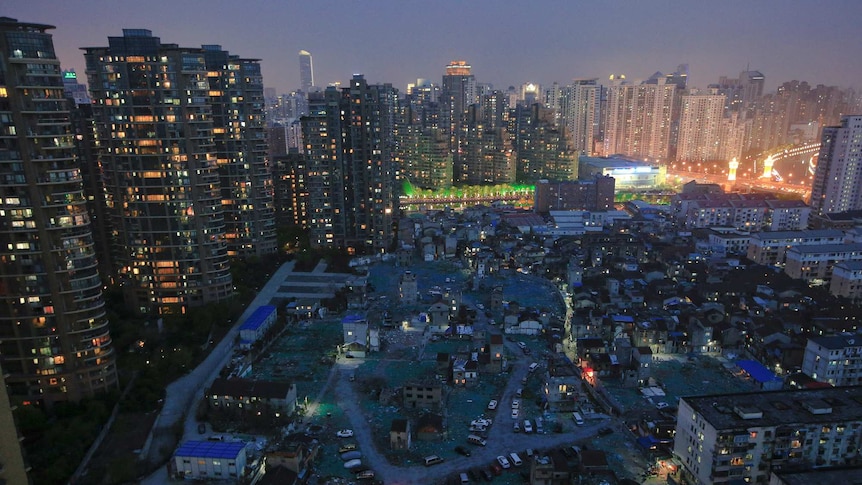 A night view of old houses surrounded by dozens of high-rise apartment buildings