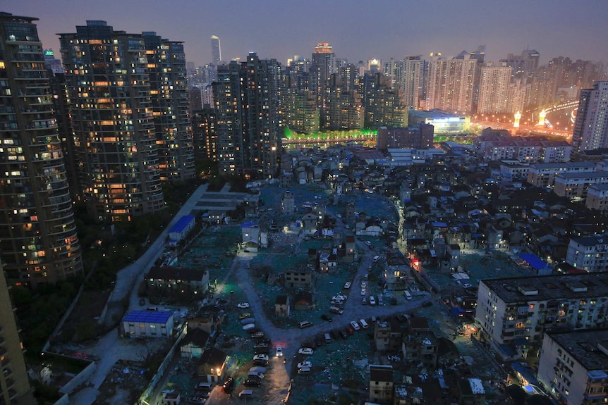 A night view of old houses surrounded by dozens of high-rise apartment buildings