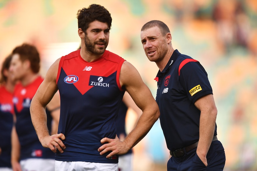 A star AFL midfielder smiles with his coach as they stand in the middle of the ground after a win.