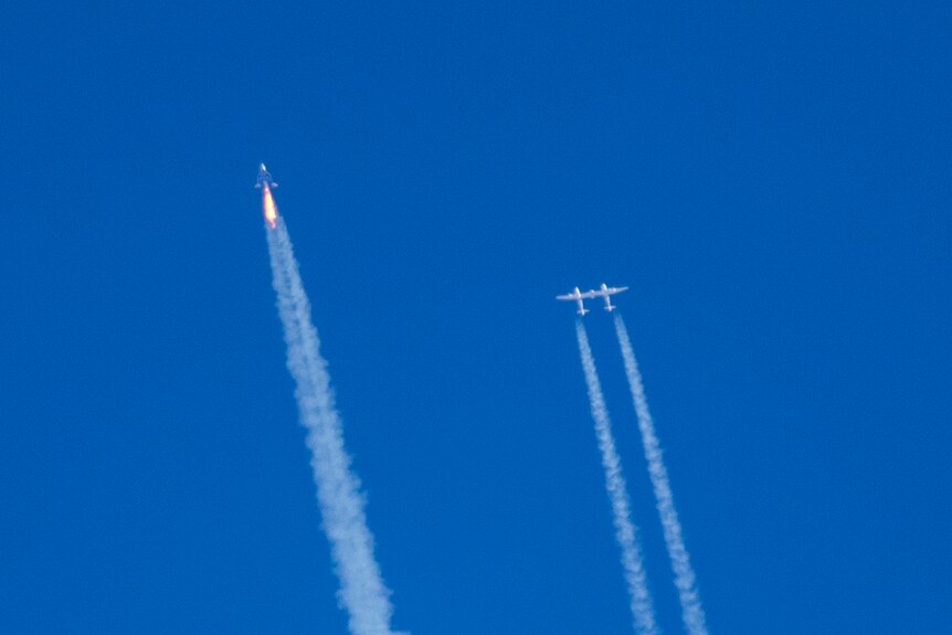 A line of smoke leading to a far away space rocket in the middle of blue sky with another plane besides it