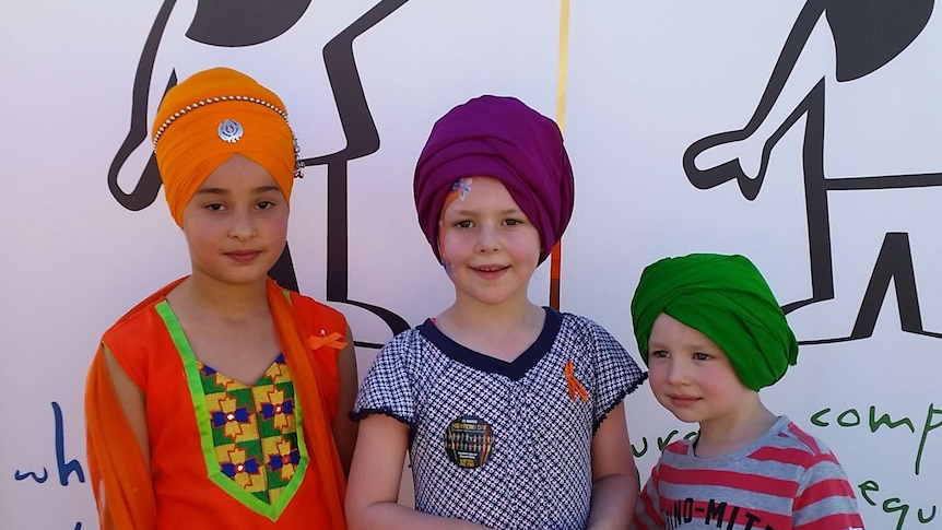Three children wearing turbans in front of a Turban and Trust sign.