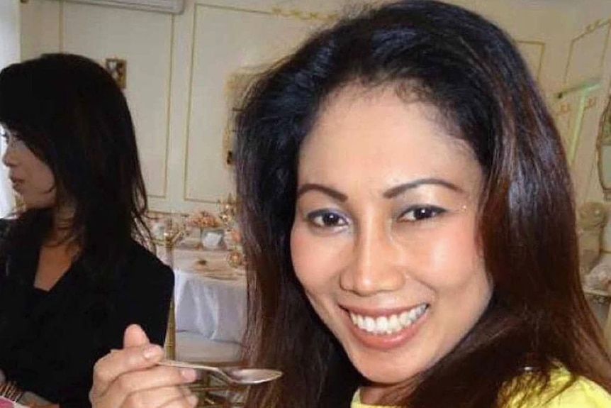 A woman in a yellow dress smiling as she eats a dessert in a restaurant