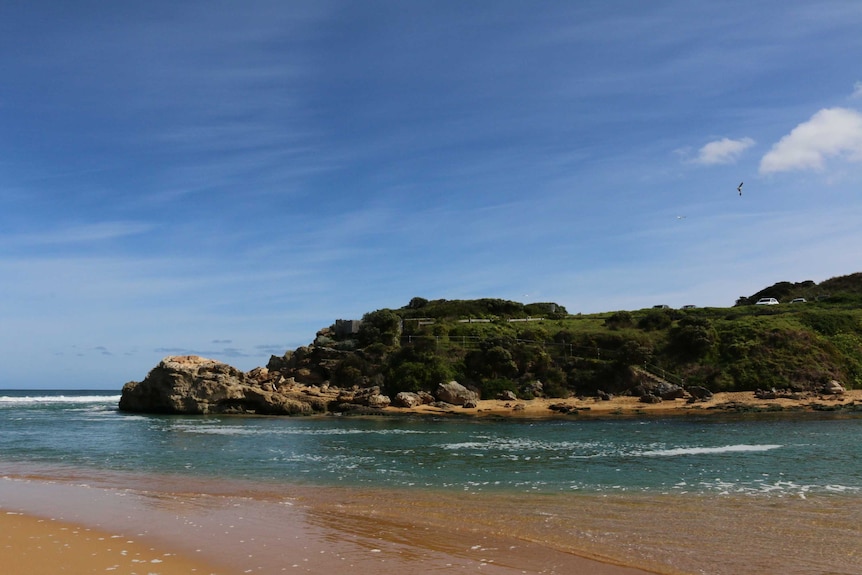 A rocky headland  with a blue sky above and a sandy beach in the foreground.