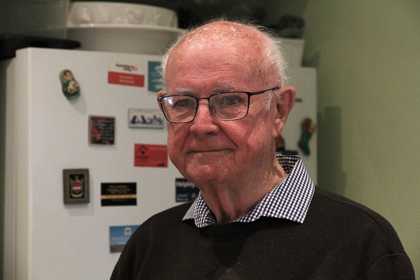 A head shot of a man with glasses standing in front of a fridge. 