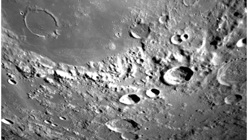 A grey and white image shows craters and ridges on the surface of the moon.