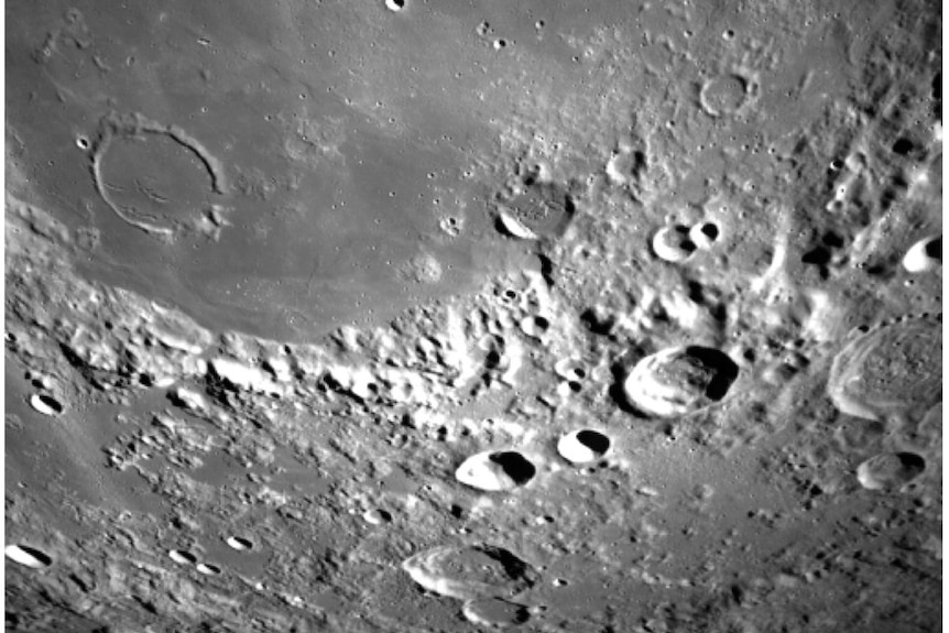 A grey and white image shows craters and ridges on the surface of the moon.