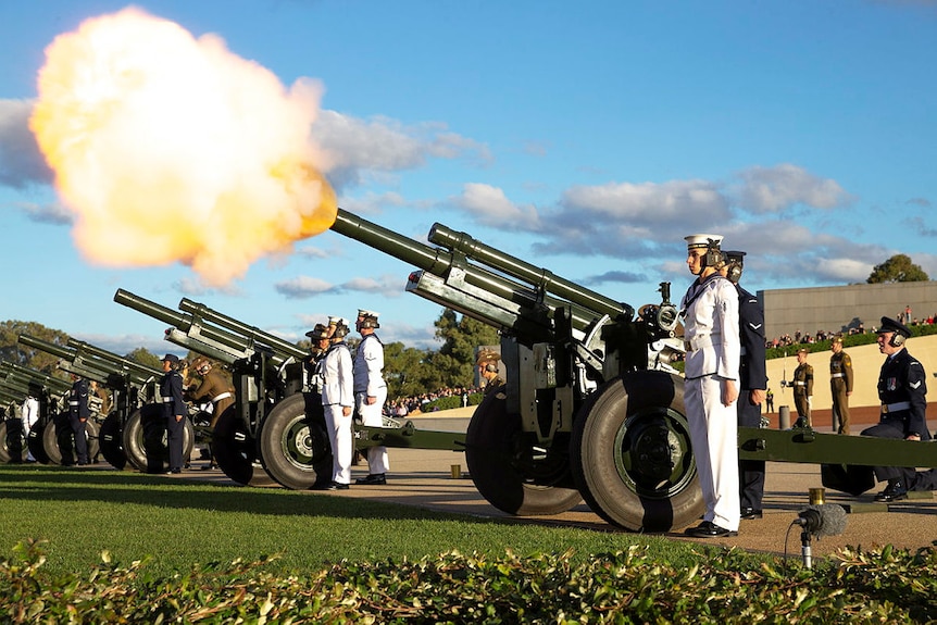 soldiers stand next to howitzers being fired on the forecourt of parliament house in the day time