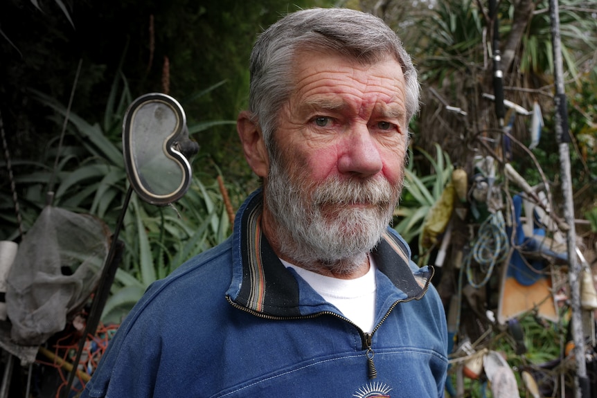 A older man with grey hair and beard is wearing a navy pullover over a white T-shirt