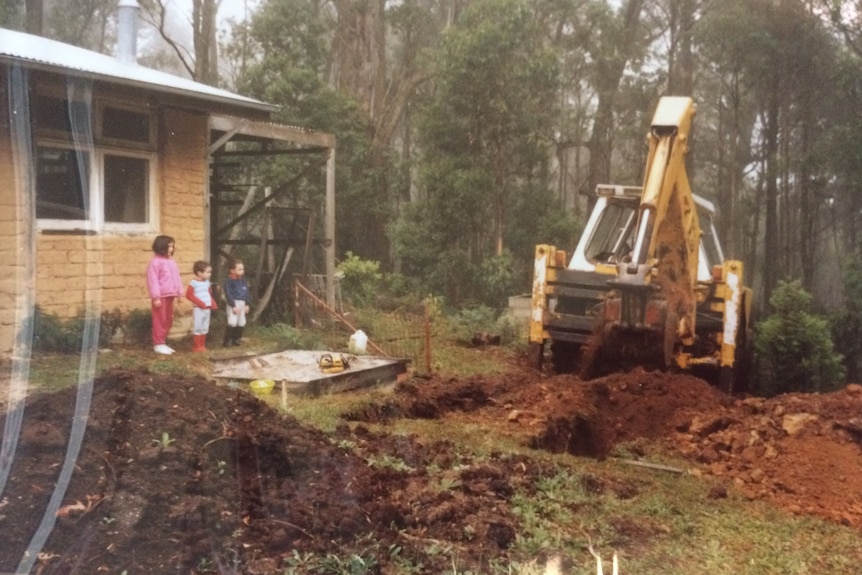 Children stand between a house and a bulldozer.
