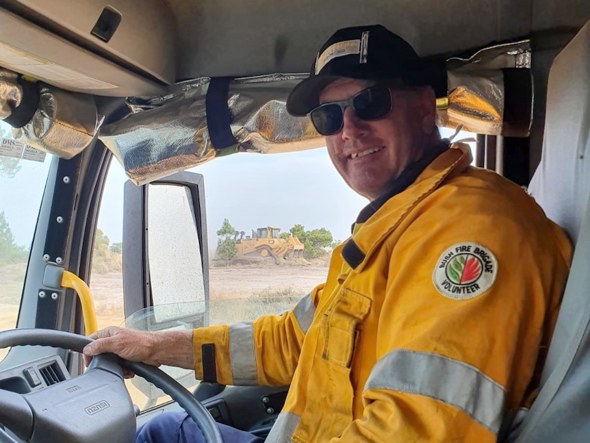 A firefighter sits in the cabin of a vehicle smiling for a photo.