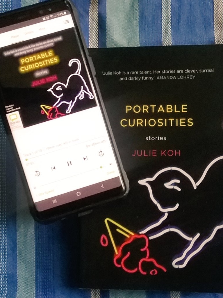 Smartphone displaying Portable Curiosities audio book next to copy of Portable Curiosities