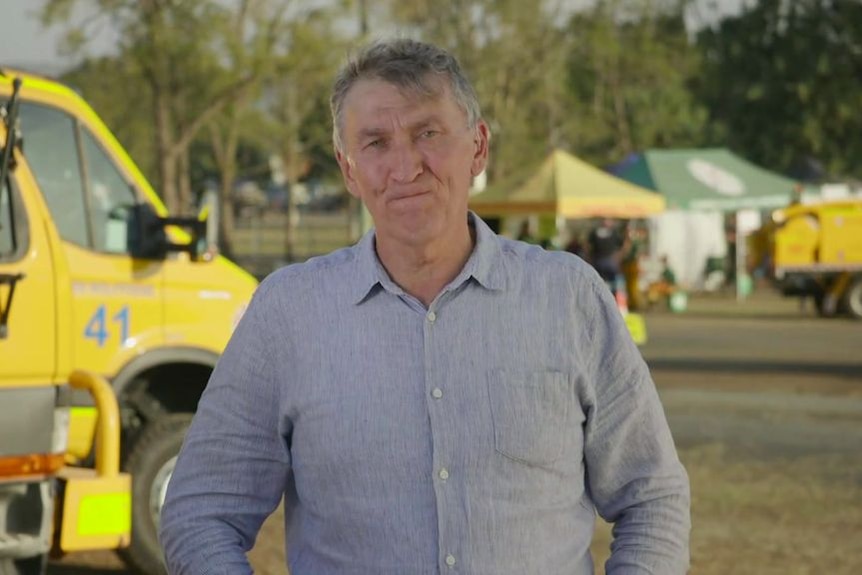 Man with grey hair standing in front of rural fire service trucks.