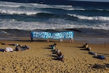 Protesters at the beach hold up a banner that says "Protect our coast from offshore gas"