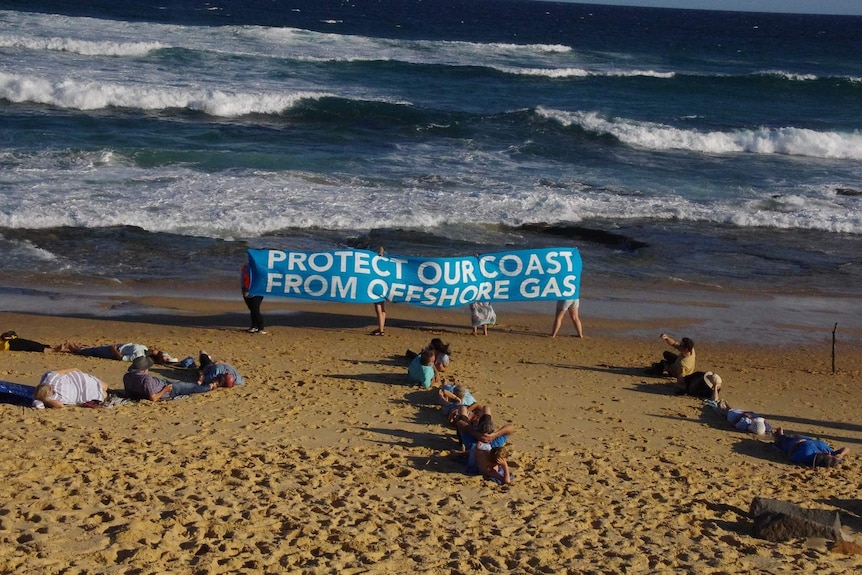 Protesters at the beach hold up a banner that says "Protect our coast from offshore gas"
