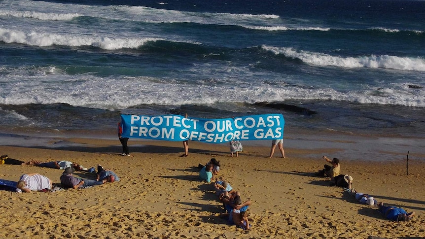 Protesters at the beach hold up a banner that says "Protect our coast from offshore gas"