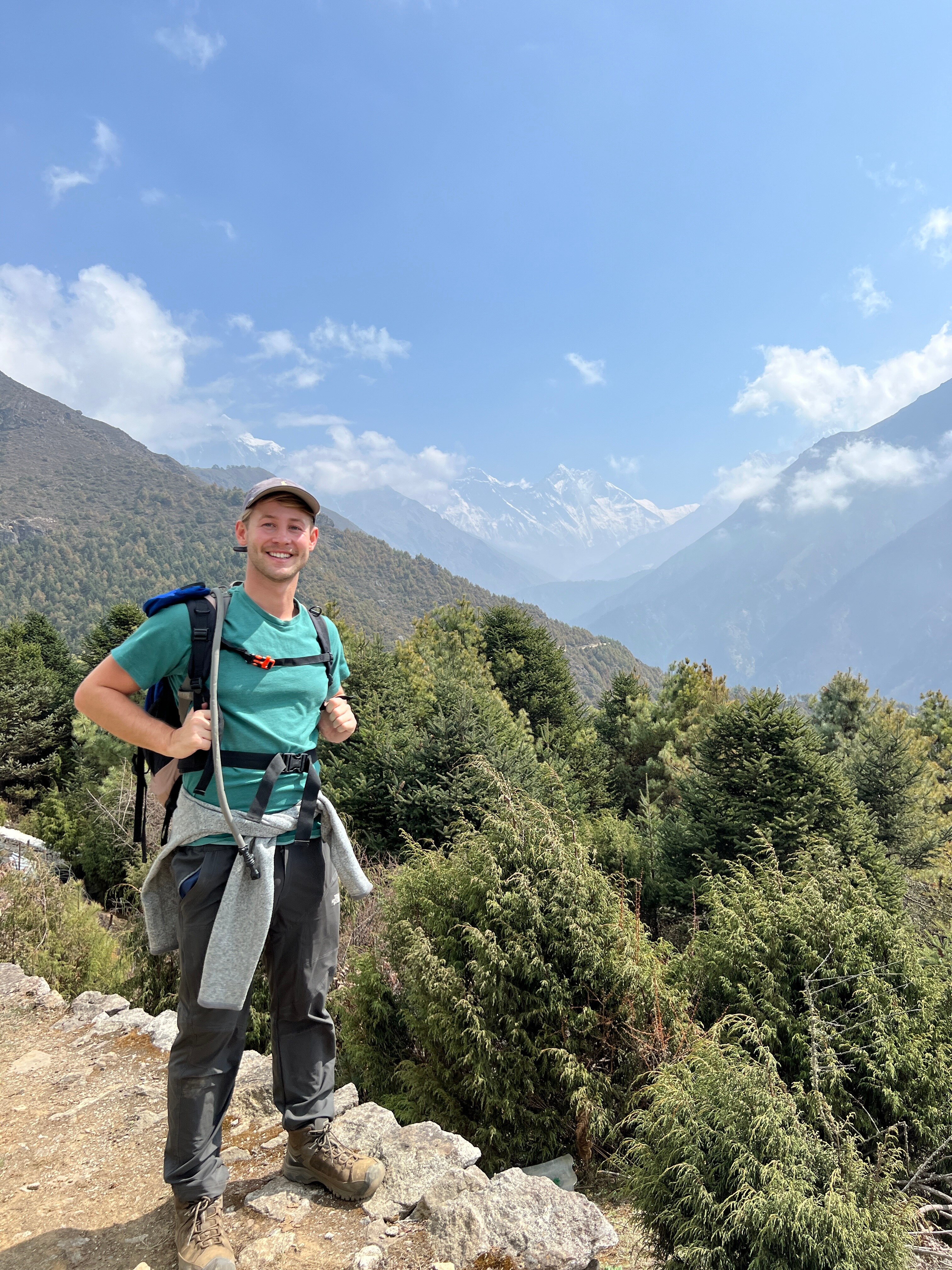 Tim Abbott hiking in a national park, with a view of mountains in the background. Wearing hiking gear and a cap.