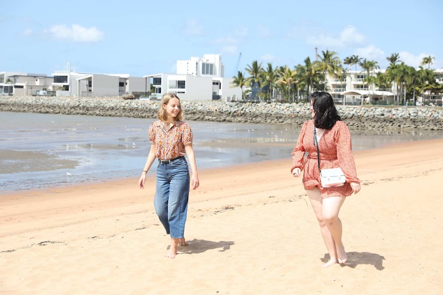 Two young woman walk down a beach on a sunny day.
