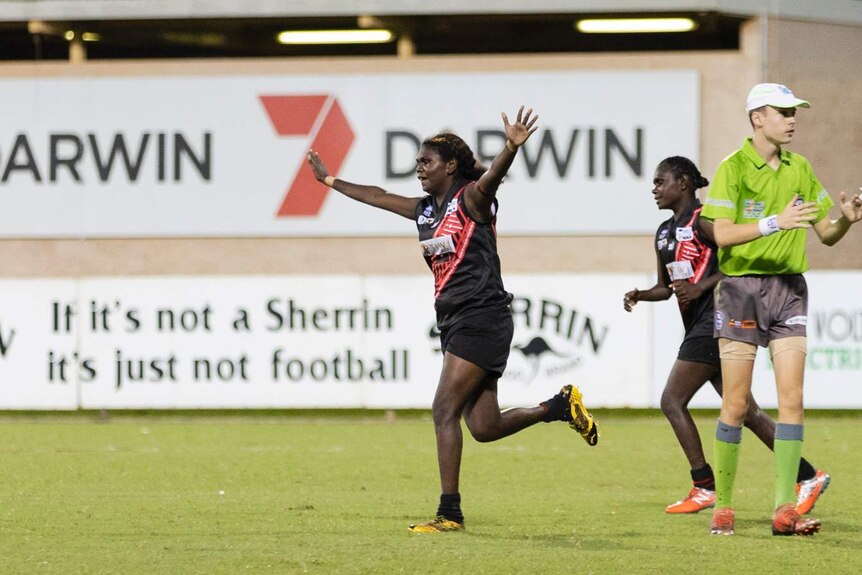 A Tiwi Bomber celebrates a goal on TIO Stadium with her hands outstretched while she runs.