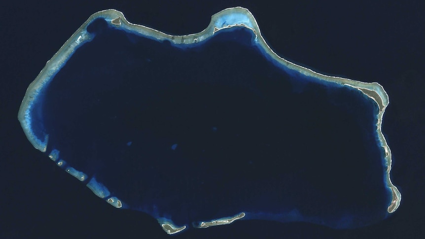 A satellite image of Bikini Atoll, appearing as a lit up ring in the blue sea.