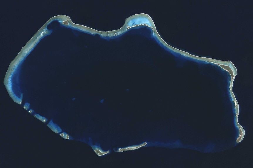 A satellite image of Bikini Atoll, appearing as a lit up ring in the blue sea.
