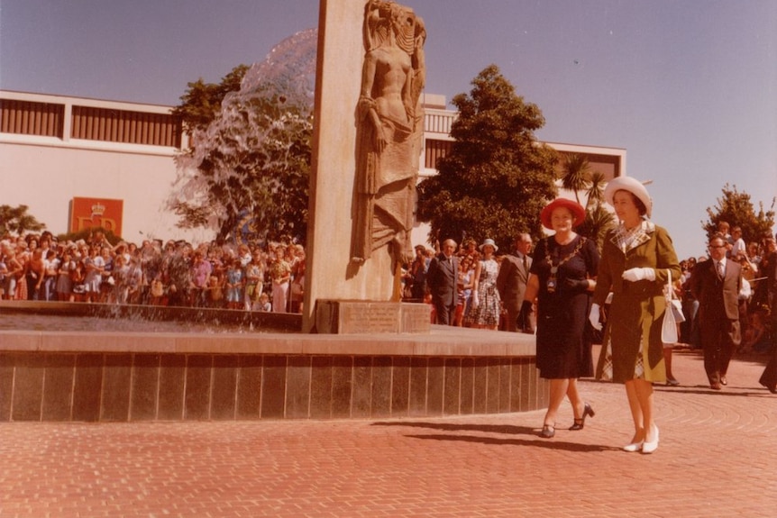 The queen walks around a fountain surrounded by a crowd of people