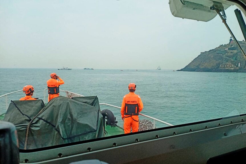 men in orange look out at sea near boat.
