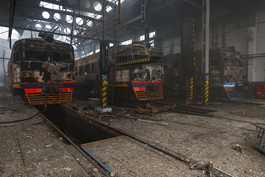 A number of burnt-out trains sit inside a burnt-out railway station.
