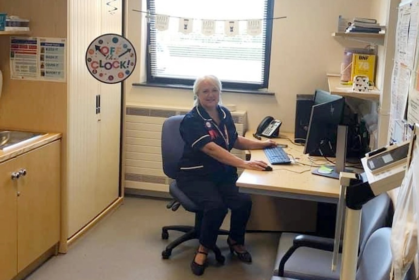 A woman in a nurse's uniform sits at a computer in an officer