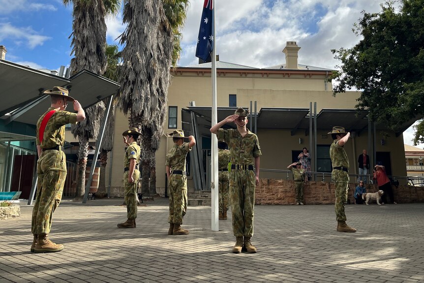 A group of army cadets stand around an Australian flag. 