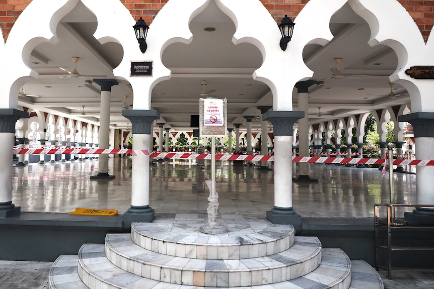 A sign stands outside a mosque with red tape around the entrances.